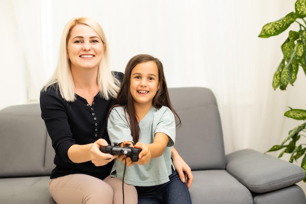 Dobry Związek ładna Dziewczynka Z Młodą Matką Za Pomocą Joysticka Grając W Gry Wideo, Siedząc Razem W Salonie, Ciesząc Się Rodzinnymi Wakacjami.