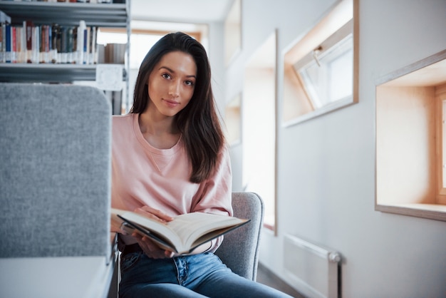 Dobrze wyglądająca kobieta. Brunetka dziewczyna w ubranie, dobra zabawa w bibliotece pełnej książek