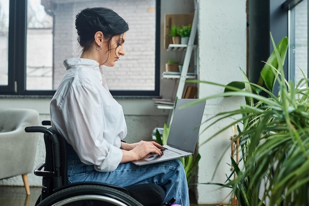 Dobrze wyglądająca, oddana kobieta biznesowa w zwykłym stroju na wózku inwalidzkim trzymająca laptop w biurze