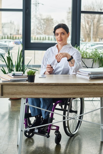 Dobrze wyglądająca, pewna siebie bizneswoman z niepełnosprawnością na wózku inwalidzkim z okularami patrzącymi na kamerę