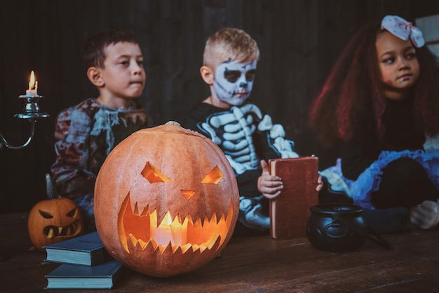 Dobrzy Mali Przyjaciele W Kostiumach Na Halloween Siedzą Na Podłodze Z Dyniami I świecami.