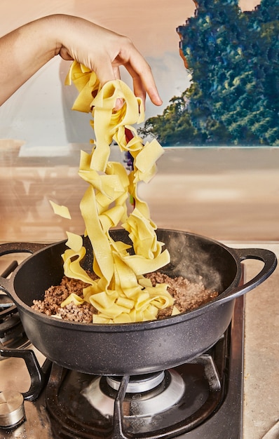 Dodaje spaghetti do mielonej wołowiny smażonej na patelni do spaghetti bolognese według przepisu z internetu.