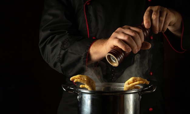 Dodanie suchego pieprzu rękami kucharza do patelni z wrzącymi nogami kurczaka Koncepcja przygotowywania dodatku lub bogatej zupy w kuchni restauracji lub hotelu