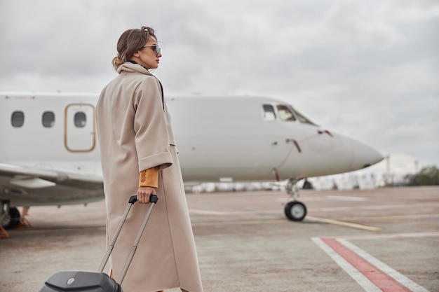 Dojrzała biznesowa kobieta w płaszczu w pobliżu odrzutowca na lotnisku