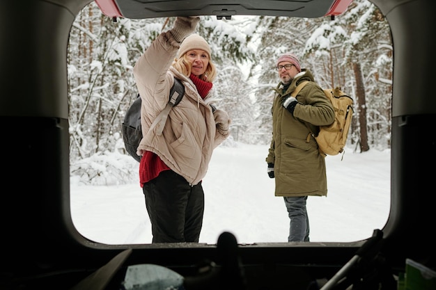 Dojrzała blond kobieta z plecakiem zamykającym bagażnik samochodu