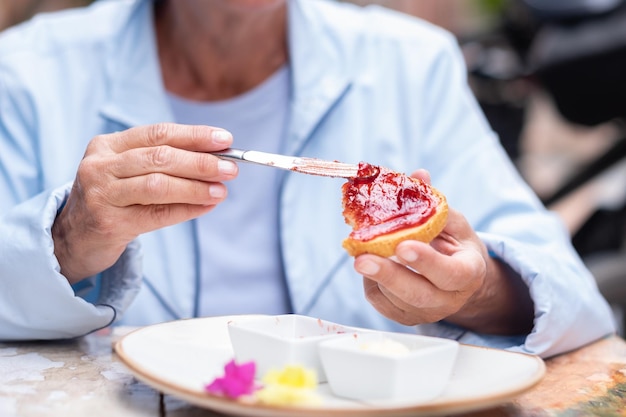 Dojrzała kaukaska kobieta siedząca przy stoliku na świeżym powietrzu rozsmarowuje dżem truskawkowy na toście Zdrowe i smaczne śniadanie lub przekąskę