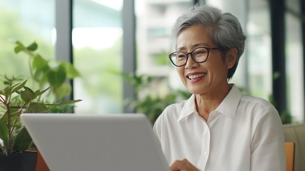 dojrzała kobieta biznesowa używająca laptopa uśmiecha się rozmawiając z przyjacielem w białym biurze