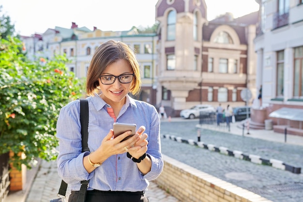 Dojrzała kobieta biznesu, pisząc na smartfonie, spacerując ulicą miasta