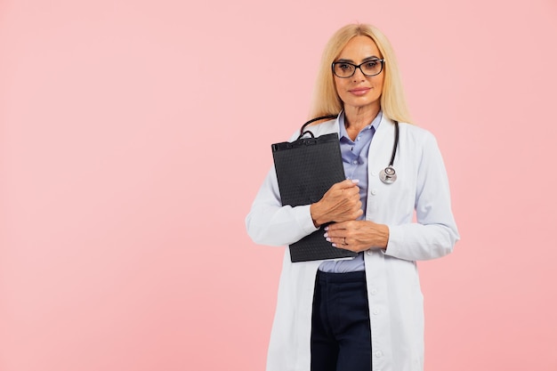 Dojrzała kobieta lekarz w okularach ze stetoskopem trzymając folder na różowym tle z miejscem na kopię