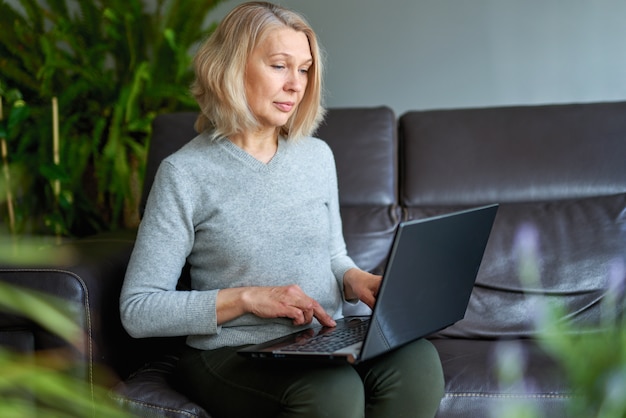 Zdjęcie dojrzała kobieta pracuje online siedzieć na kanapie w domu