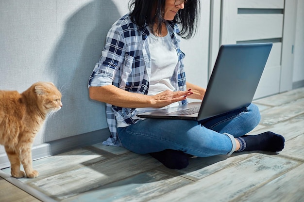Dojrzała kobieta przeszukuje stronę weterynaryjną na laptopie, aby zarejestrować kota na konsultację weterynaryjną
