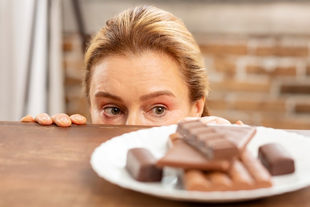 dojrzała kobieta ukrywająca się i patrząca na ciemną czekoladę, ale ma alergię