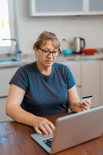 Dojrzała kobieta używająca karty kredytowej dokonująca płatności online w domu