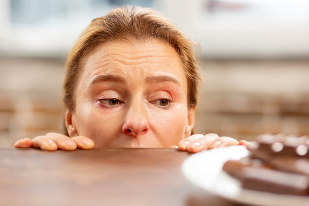 dojrzała kobieta z alergią patrząca na czekoladę leżącą na stole