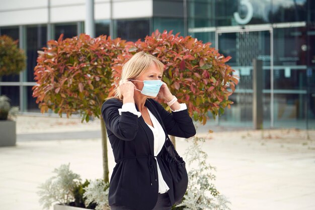 Dojrzała kobieta zakładająca maskę PPE Spacer na zewnątrz po ulicy podczas pandemii zdrowia