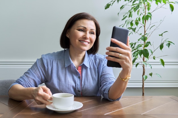 Dojrzała Kobieta Ze Smartfonem Siedzi W Domu Uśmiechając Się Patrząc Na Ekran Telefonu