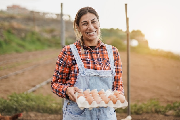 Dojrzała latynoska kobieta trzymająca świeże jajka - starszy rolnik uśmiechający się do kamery