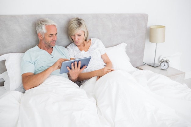Dojrzała para używa cyfrową pastylkę w łóżku