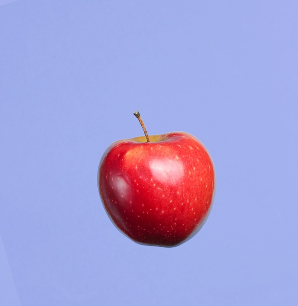 Dojrzałe czerwone jabłko na niebieskim tle.