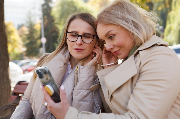 Dojrzałe kobiety korzystające ze słuchawek ze smartfonem na zewnątrz