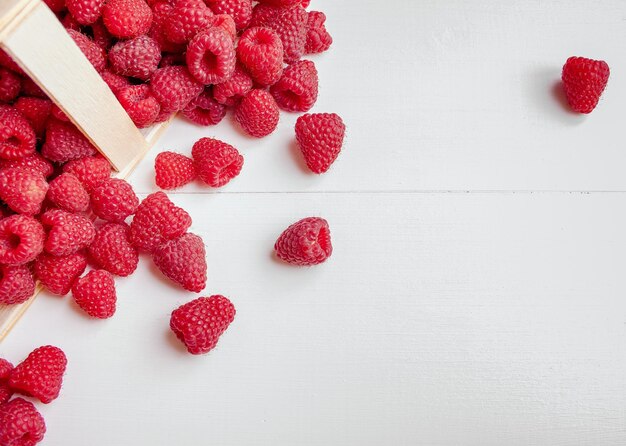 Zdjęcie dojrzałe organiczne maliny w koszu z brzozy na białym drewnianym tle