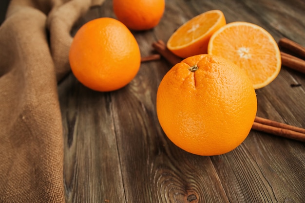 Dojrzałe soczyste pomarańcze na starej drewnianej stole kopiują przestrzeń. Połówki pomarańczy. Laski cynamonu