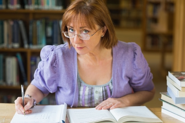 Dojrzałe studenckie writing notatki przy biurkiem w bibliotece