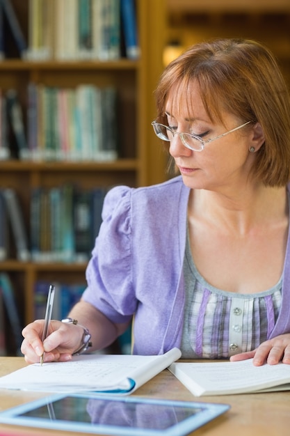 Dojrzałe studenckie writing notatki przy biurkiem w bibliotece