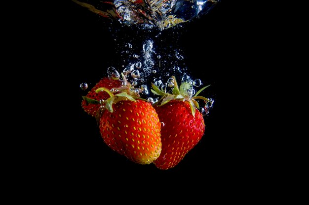 Dojrzałe truskawki wpadają do wody, unosząc bryzgi i bąbelki powietrza