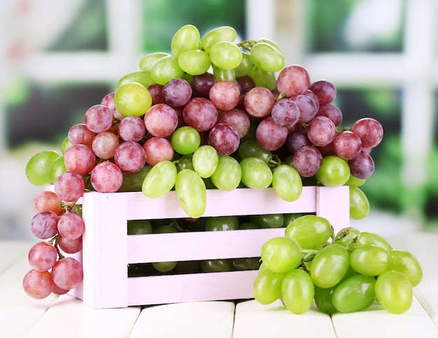 Dojrzałe zielone i fioletowe winogrona w drewnianym pudełku na drewnianym stole na naturalnym tle