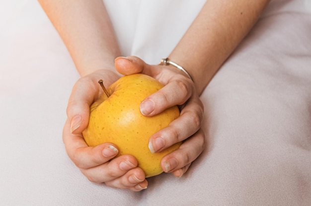 Dojrzałe żółte jabłko w delikatnych kobiecych rękach
