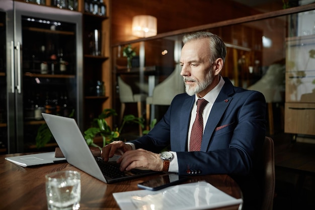 Dojrzały biznesmen pracuje na laptopie w kawiarni