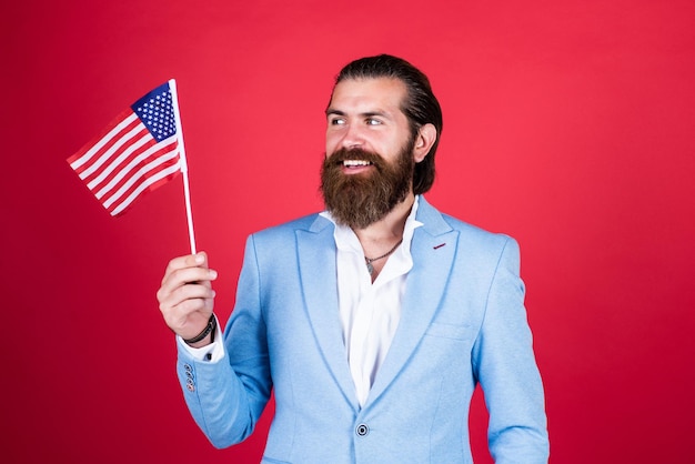 Dojrzały, brodaty mężczyzna wyglądający elegancko, trzymający flagę narodową amerykańskiego polityka