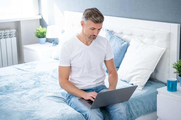 Dojrzały facet używający komputera w łóżku z kawą
