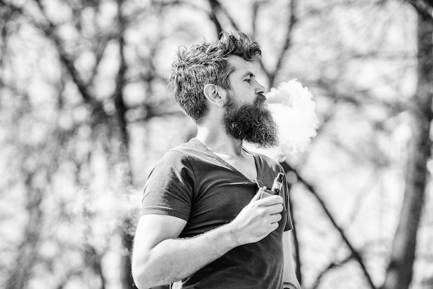 Dojrzały hipster z brodą hipster mężczyzna trzymać urządzenie do waporyzacji Bezpieczeństwo zdrowotne i uzależnienie wdychanie oparów palenie e-papieros Brodaty brutalny mężczyzna palący elektroniczny papieros Portret męskości