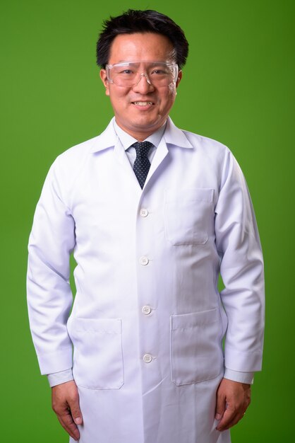Dojrzały japoński lekarz mężczyzna w okularach ochronnych na zielonym tle
