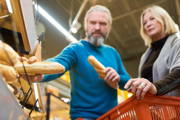 Dojrzały mężczyzna, który bierze dwie świeże pszenne bagietki z półki w supermarkecie