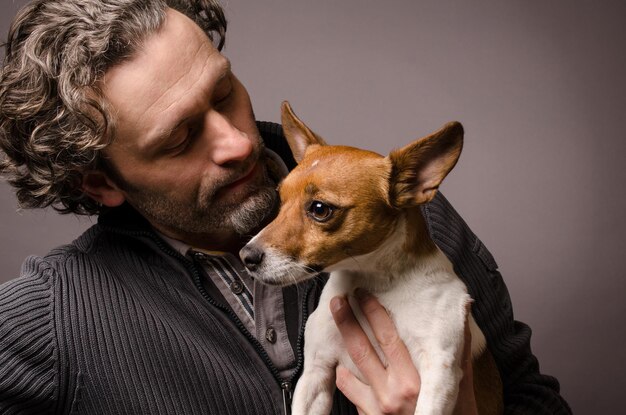 Dojrzały mężczyzna niosący jack russell terriera na szarym tle