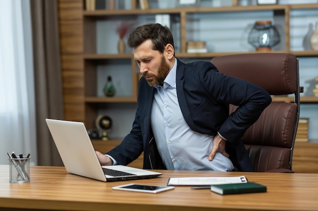 Dojrzały mężczyzna pracujący w nowoczesnym biurze z laptopem, starszym szefem, który ma poważny ból pleców, biznesmen o godz