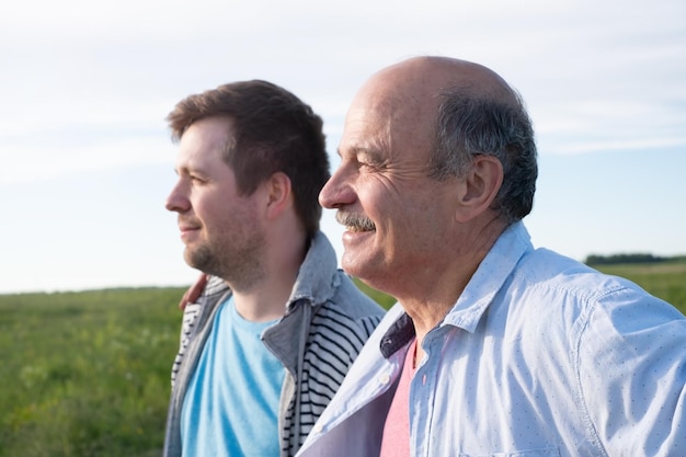 Dojrzały ojciec rasy kaukaskiej i jego syn patrzą z boku na aparat stojący w polu