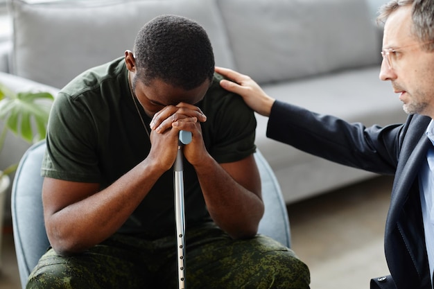 Dojrzały psycholog pocieszający i wspierający czarnego żołnierza podczas leczenia ptsd podczas sesji terapeutycznej