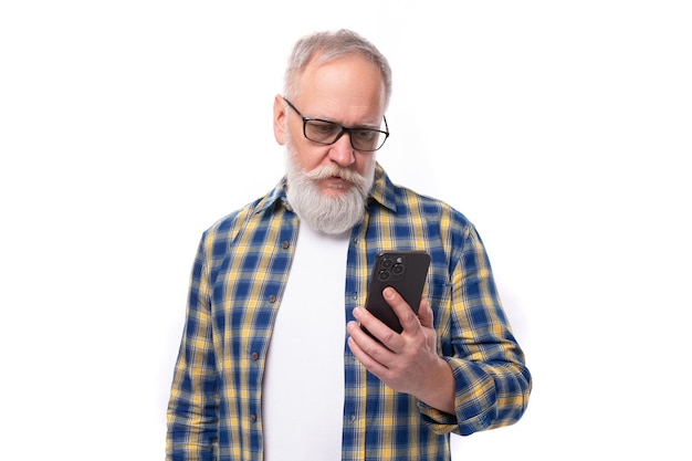 Dojrzały siwowłosy emeryt z wąsami i brodą opanowuje technologię smartfonów na białym