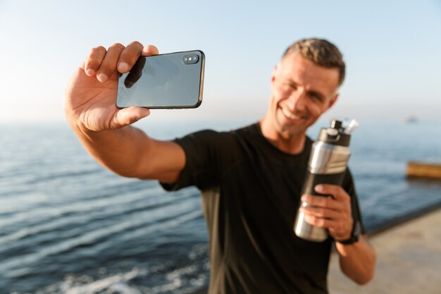 Dojrzały Sportowiec Robi Selfie Z Butelką Wody Na Plaży.