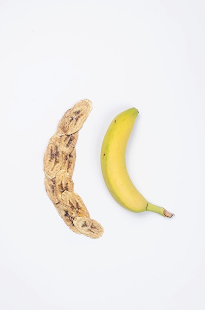 Dojrzały surowy banan i suszone plasterki bananów żetony rozrzucone na białym tle. Chipsy owocowe. Koncepcja zdrowego odżywiania, przekąska, bez cukru. Widok z góry, kopia przestrzeń.