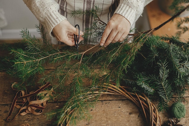 Dokonywanie wieniec bożonarodzeniowy w stylu rustykalnym Kobiece ręce tnące gałęzie jodły nożyczkami