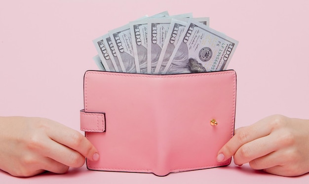 Dolary i różowy portfel w ręku kobiety na różowym tle z przestrzenią do kopiowania