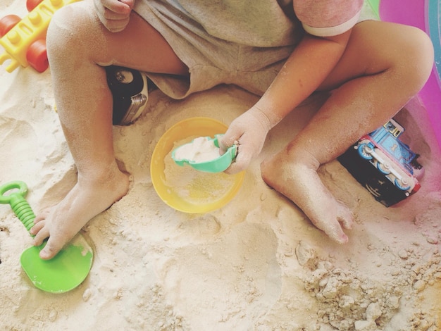 Zdjęcie dolna część chłopca bawiącego się zabawkami siedzącego na piasku na plaży