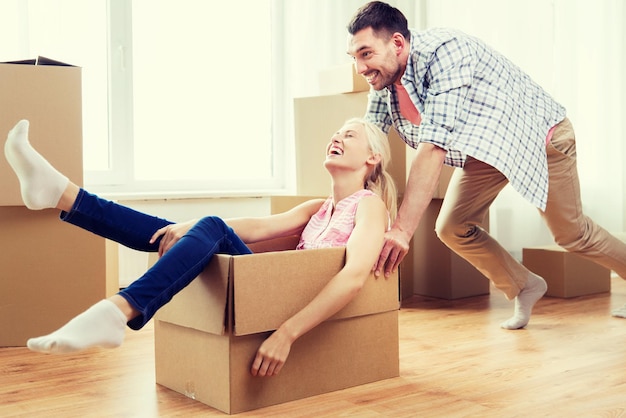 dom, ludzie, przeprowadzki i koncepcja nieruchomości - szczęśliwa para bawi się i jeździ w kartonowych pudełkach w nowym domu