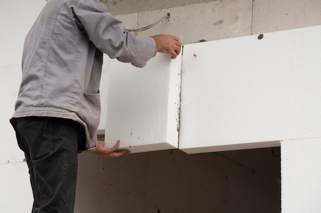 Dom ocieplony. Pracownik budowlany izolujący ścianę domu za pomocą styropianowej płyty izolacyjnej