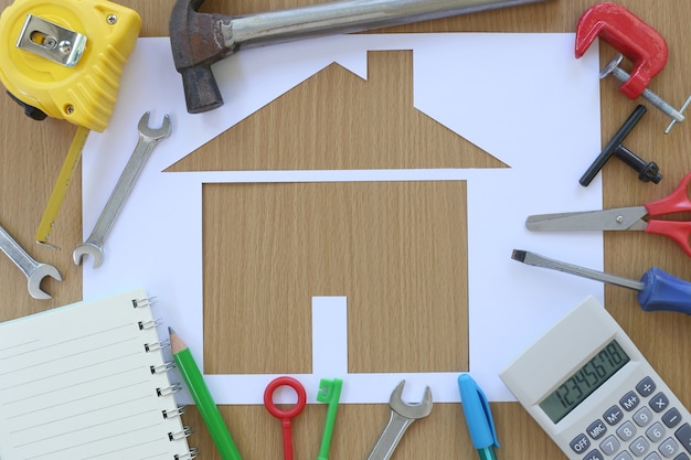 Dom w kształcie papieru na tle brązowego drewna i narzędzia Craftsman.
